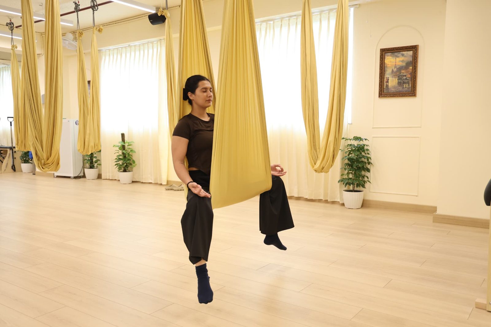 Woman supported in a fabric aerial yoga hammock in the sunlit studio