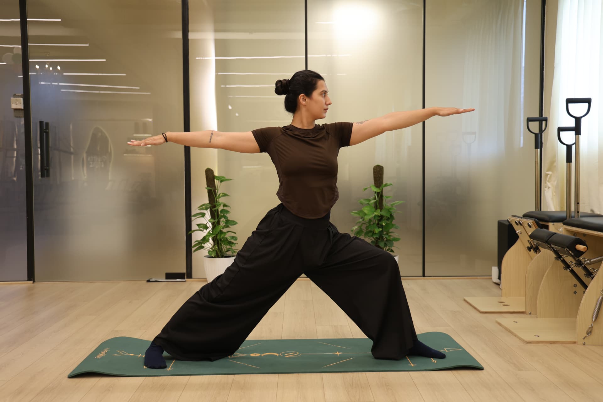 Woman holding a standing hatha yoga pose on a mat in the sunlit studio
