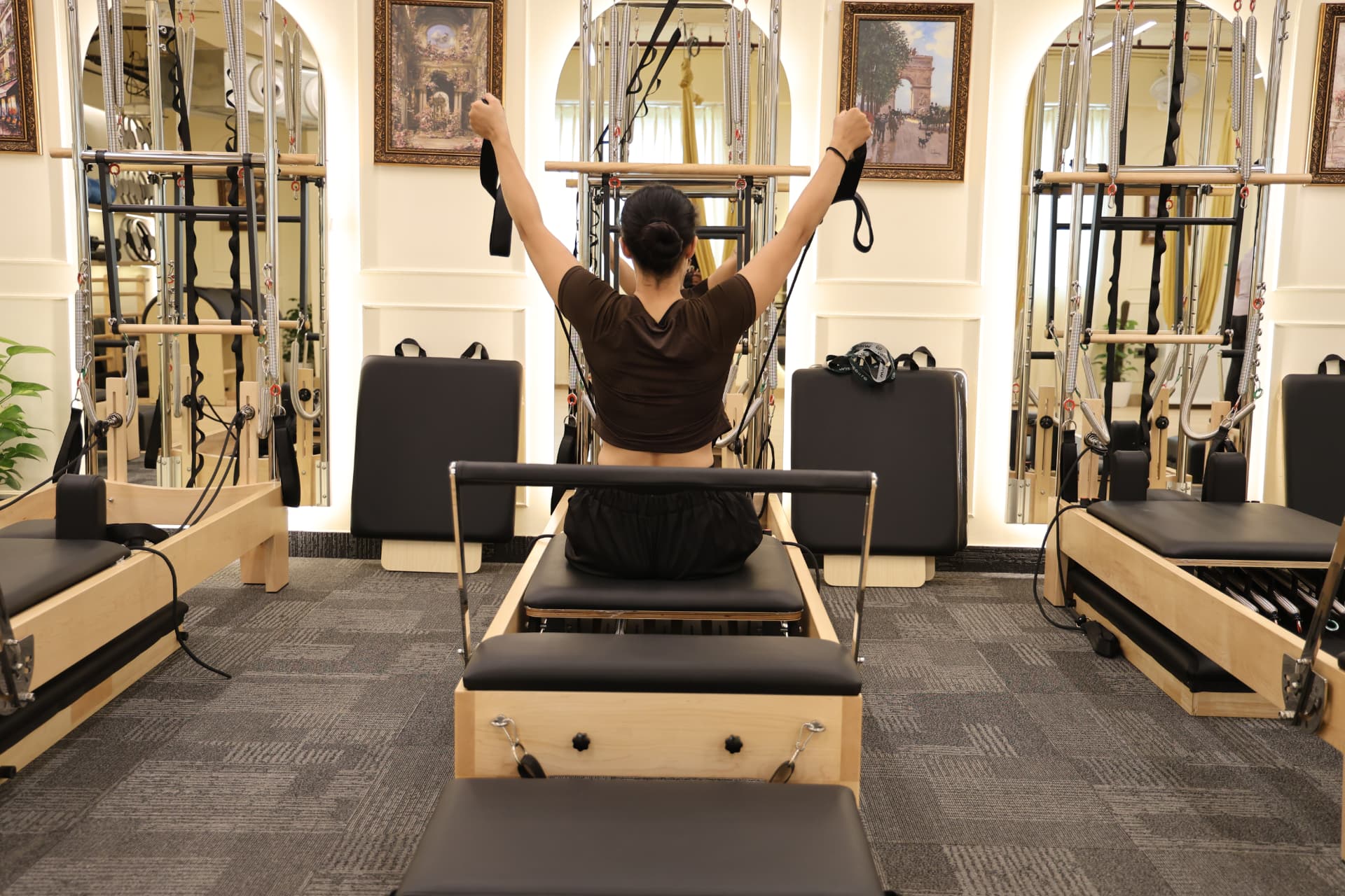A member training on a reformer with straps overhead at the Raj Nagar Extension studio