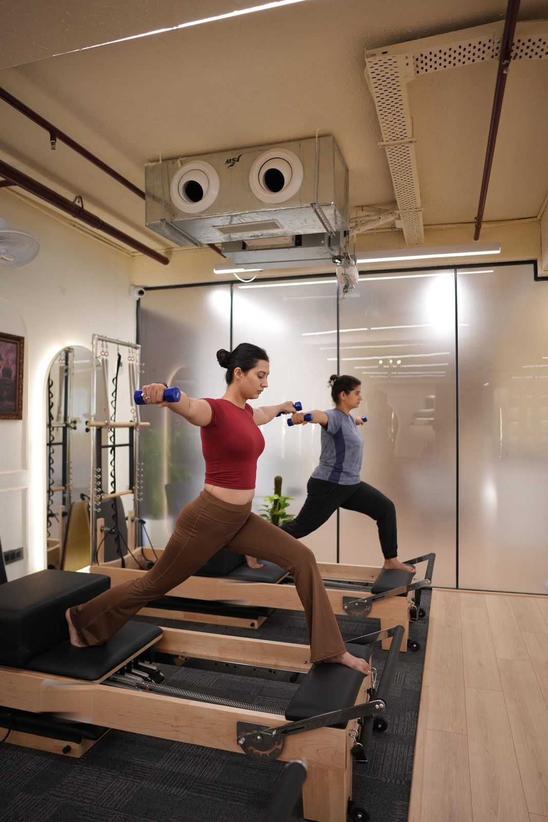 Two clients in a standing lunge on the reformers with hand weights