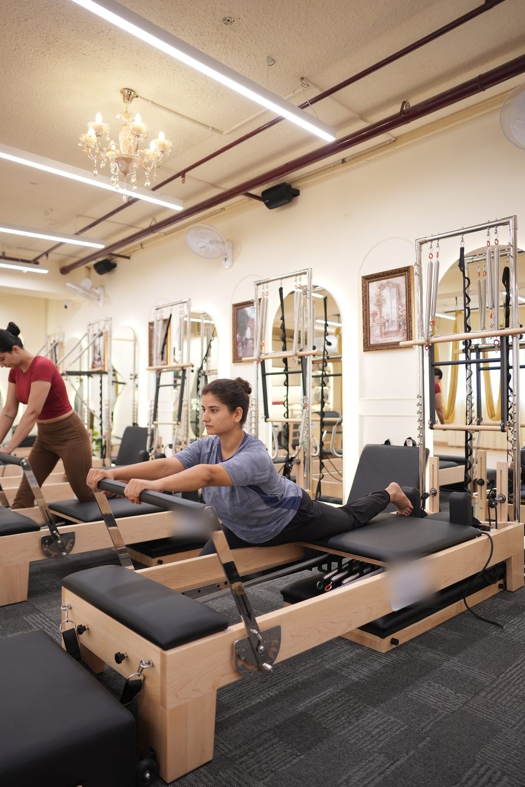 Two clients on the reformers during an arm series under the studio chandelier